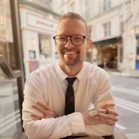 Jaxon Peterson, seated at a cafe table, arms crossed, smiling.